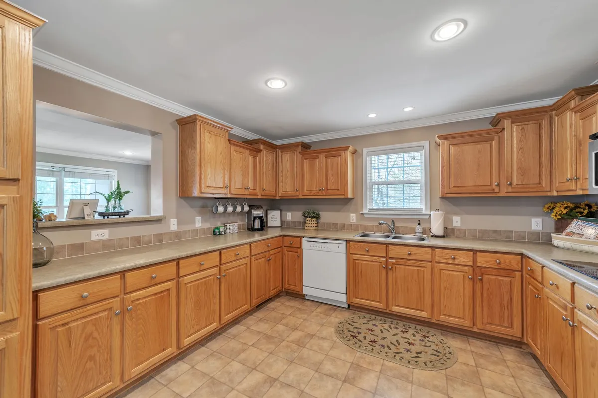 A spacious kitchen illuminated by natural light pouring through a window. Rich wooden cabinetry lines the walls and a generous kitchen island sits at the center, providing plenty of prep and gathering space. The scene radiates warmth and is set up for cooking, family gatherings, and entertaining guests.