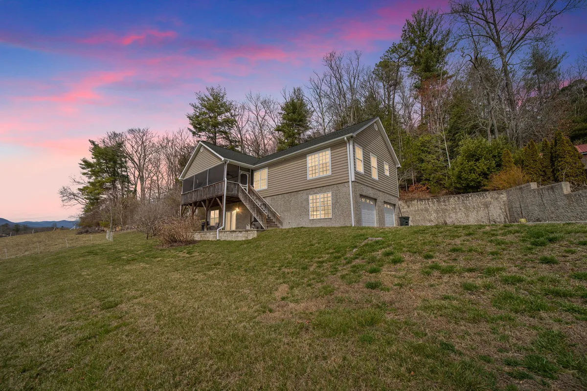 The image showcases the exterior of a charming single-family house nestled among lush trees, with a welcoming porch perfectly positioned to capture breathtaking sky colors at sunset. The tranquil setting hints at opportunities for outdoor gatherings, soaking in nature, and stargazing, all framed by the serenity of surrounding mountains and forest.