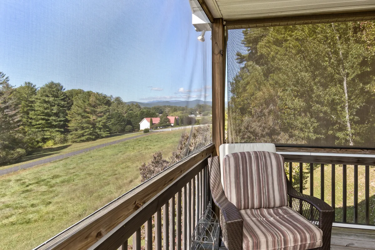 A serene screened porch featuring a comfortable rocking chair, with a breathtaking view of the mountains framed by the porch screen. The setting conveys a relaxing atmosphere perfect for lounging, reading, or enjoying a quiet beverage while immersed in nature.