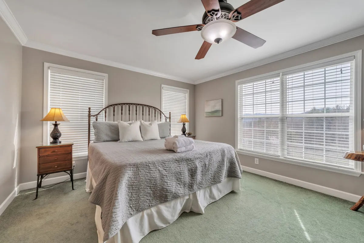 A light-filled bedroom featuring a comfortable bed with decorative pillows, nightstands with matching lamps, and expansive windows that let in morning sunlight. The calming palette and plush bedding create an inviting, restful atmosphere ideal for unwinding after a day of adventure.