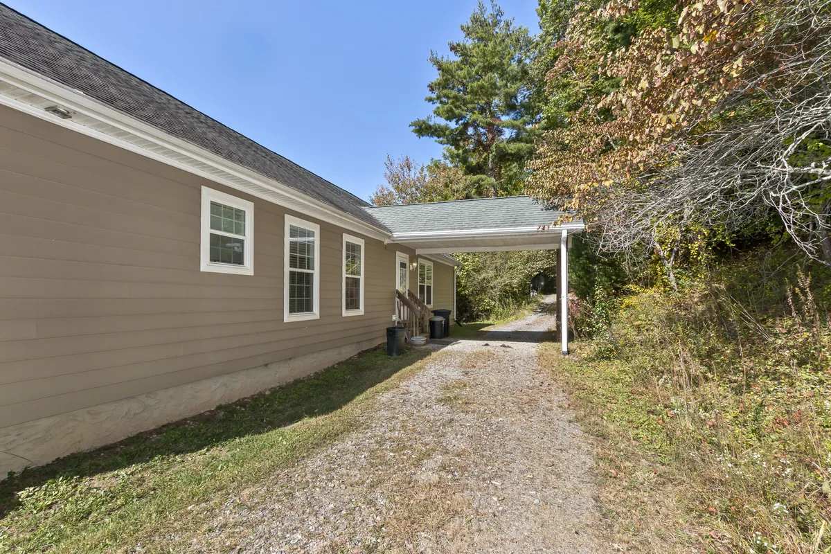 This image features the facade of the house, a welcoming driveway, and mature trees surrounding the property. The gentle slope and natural setting suggest peace and privacy, while the soft light hints at the possibility of sunrise or sunset.