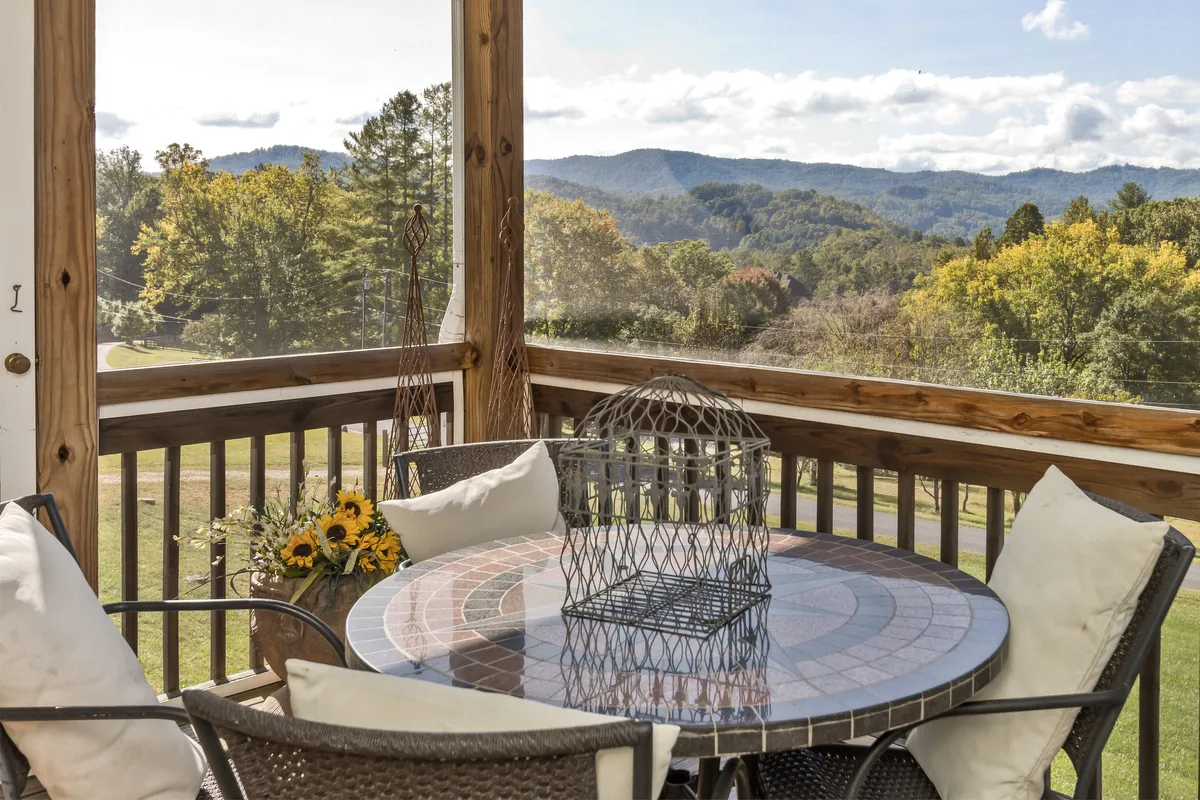 A close-up of a table adorned with a decorative cage and a cheerful sunflower arrangement, positioned to take full advantage of the sweeping mountain view. The scene communicates a relaxed and inviting mood ideal for morning coffees or sunset toasts.